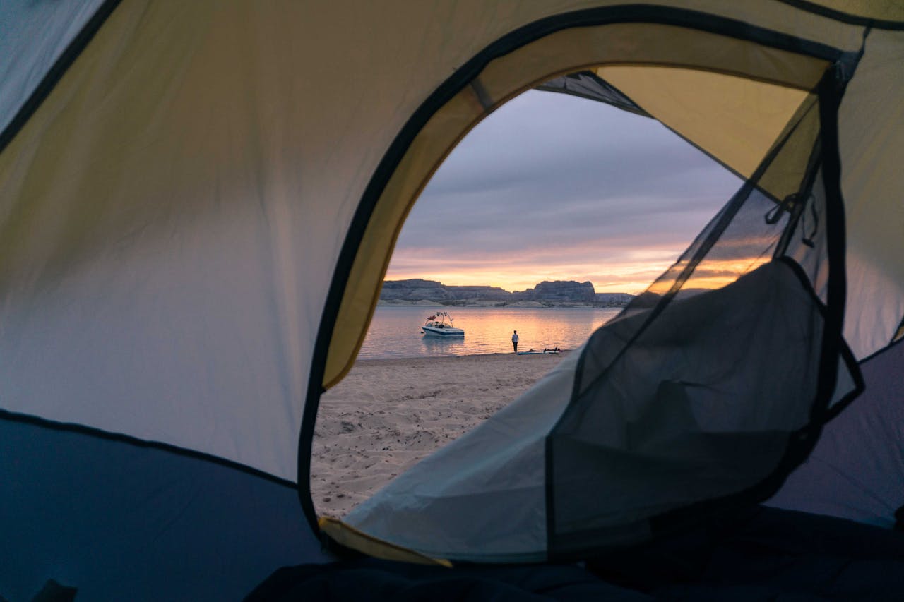 View of sandy beach with calm sea and vessel on water surface through opened tent at sunset time in nature
